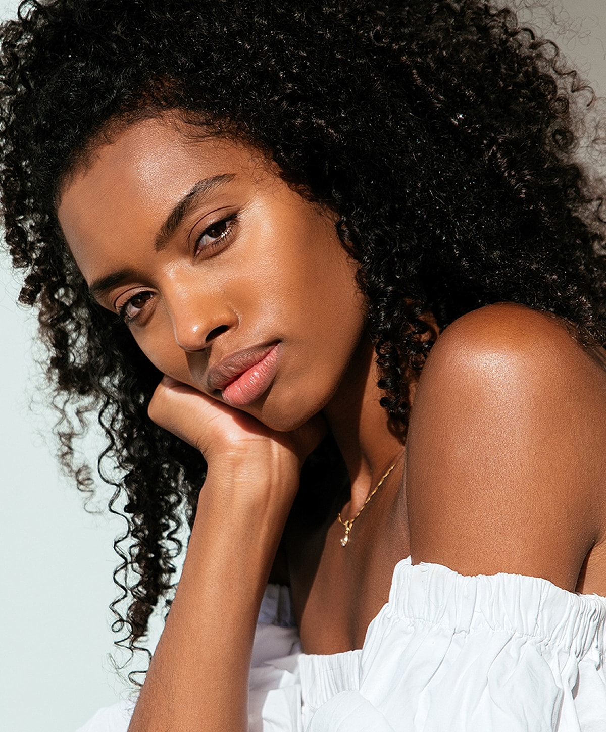 Woman with curly hair resting her chin on hand.